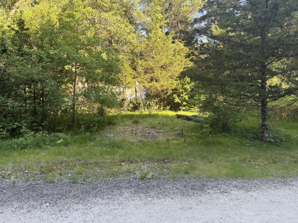 A grassy clearing set back from the gravel trail, surrounded by trees, before any construction