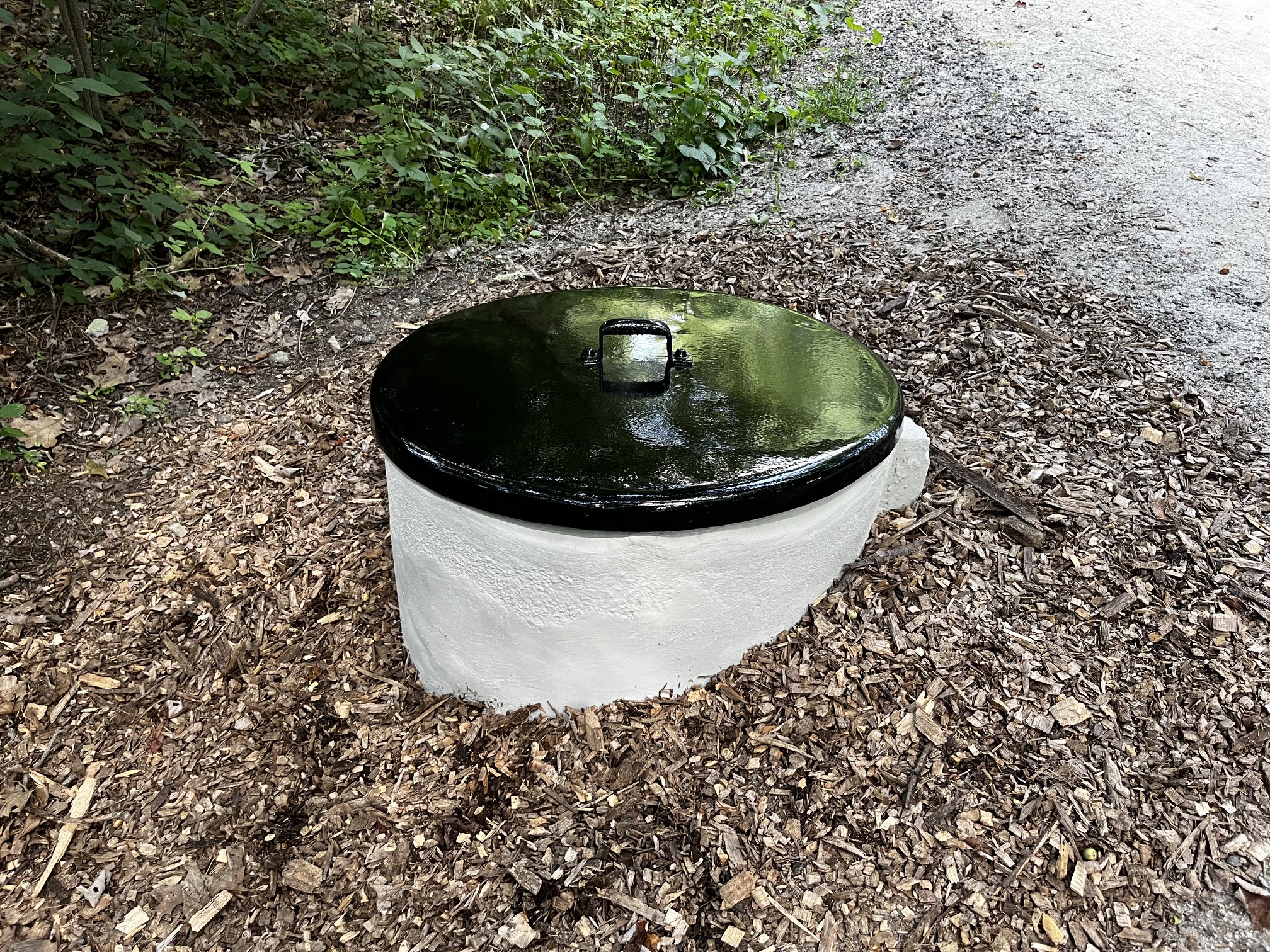 The restored battery well beside the trail, its concrete chamber painted gray and its restored metal lid painted gloss black