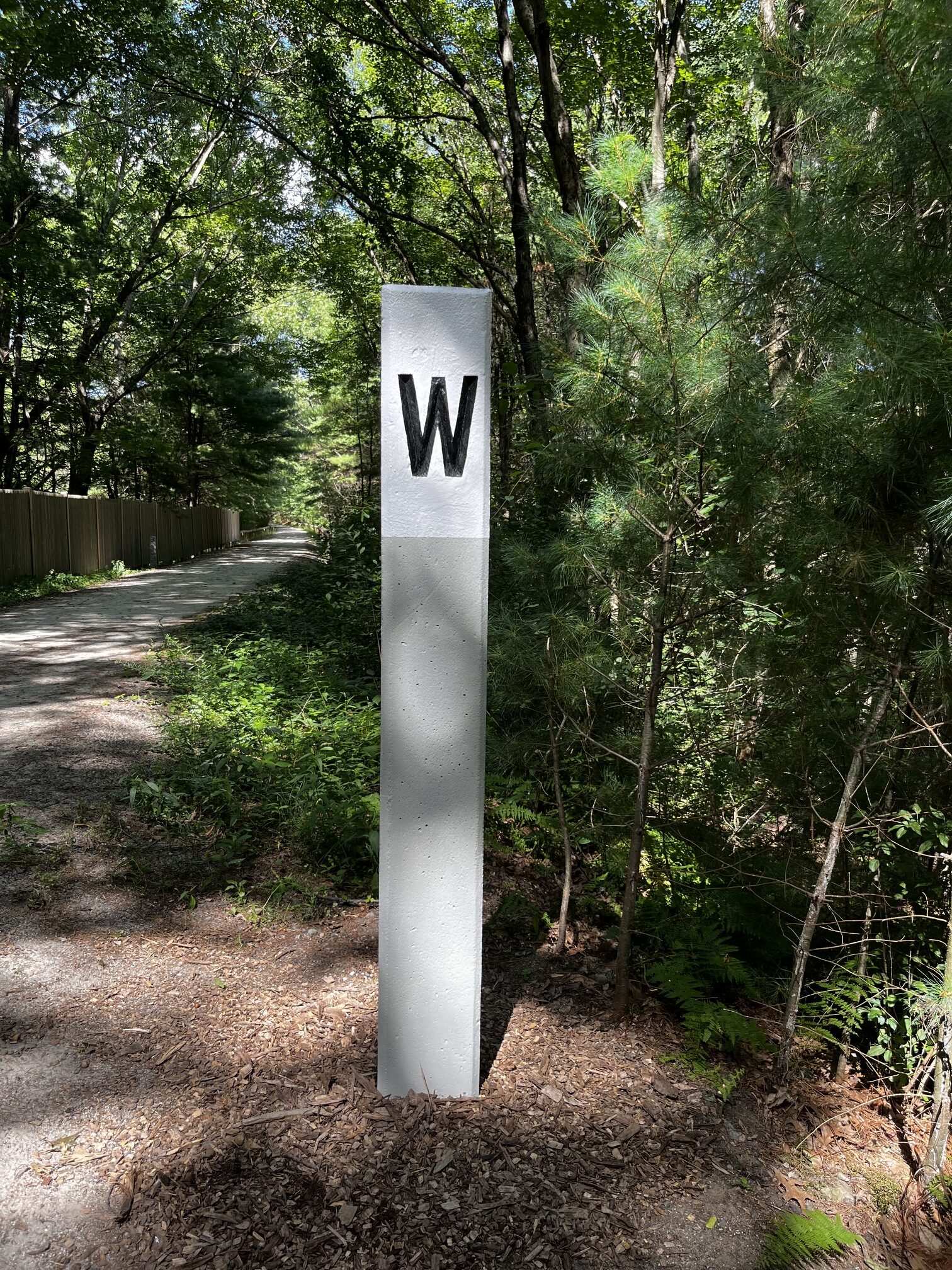 The restored whistle post standing in a fresh bed of wood chips beside the trail, with a boardwalk in the background