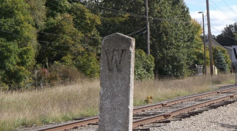 A weathered concrete whistle post standing in gravel beside an active railroad track